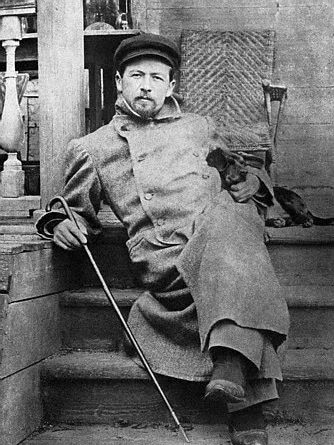 A black and white photo of a young Chekhov in a greatcoat and a bus driver's hat, lounging on a verandah.
