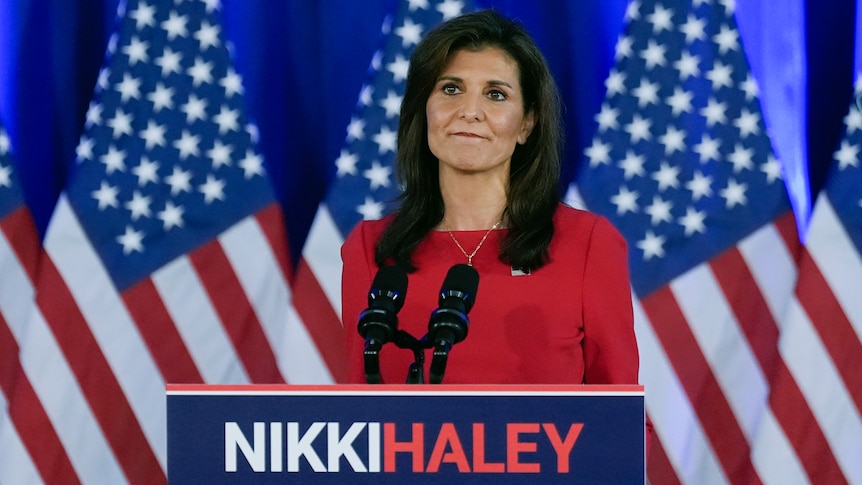 Nikki Haley stands at a podium bearing her name in front of a row of American flags.