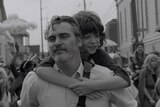 Black and white image of middle-aged man with beard wearing white shirt and giving young boy a piggyback on crowded street