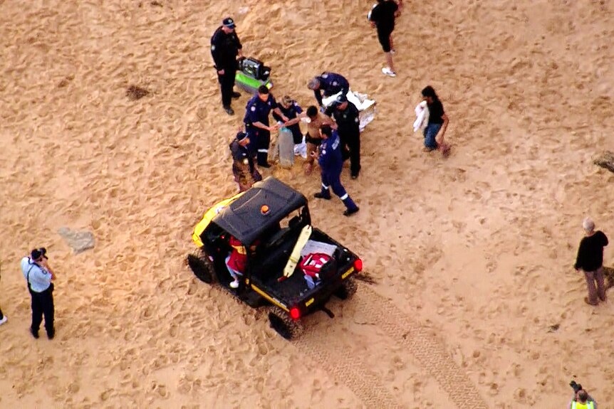 a man is help up by police and put into a buggy after being rescued from the ocean 
