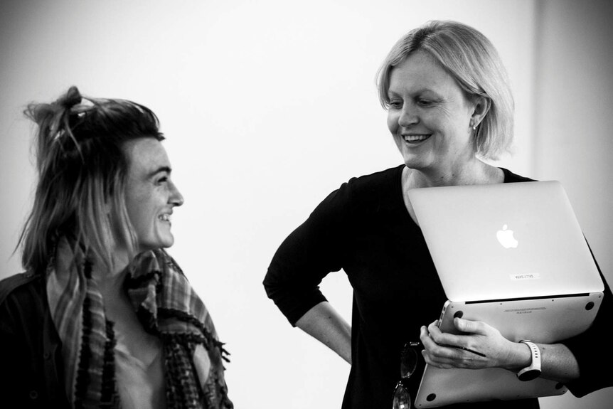 Black and white photo of Sara holding laptop laughing with another woman.