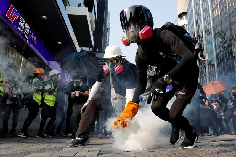 Protesters with mask holding up tear gas cannisters.