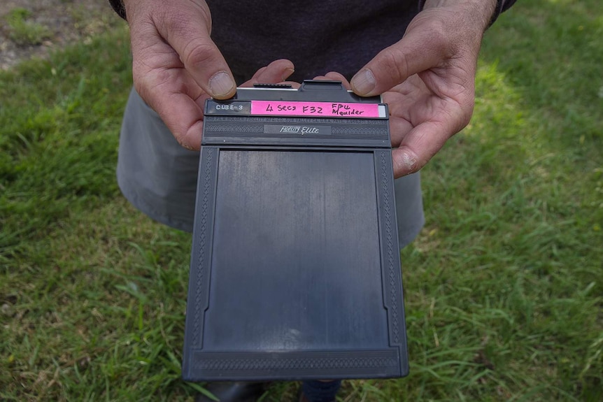 A man's hands holding a large analogue film negative.