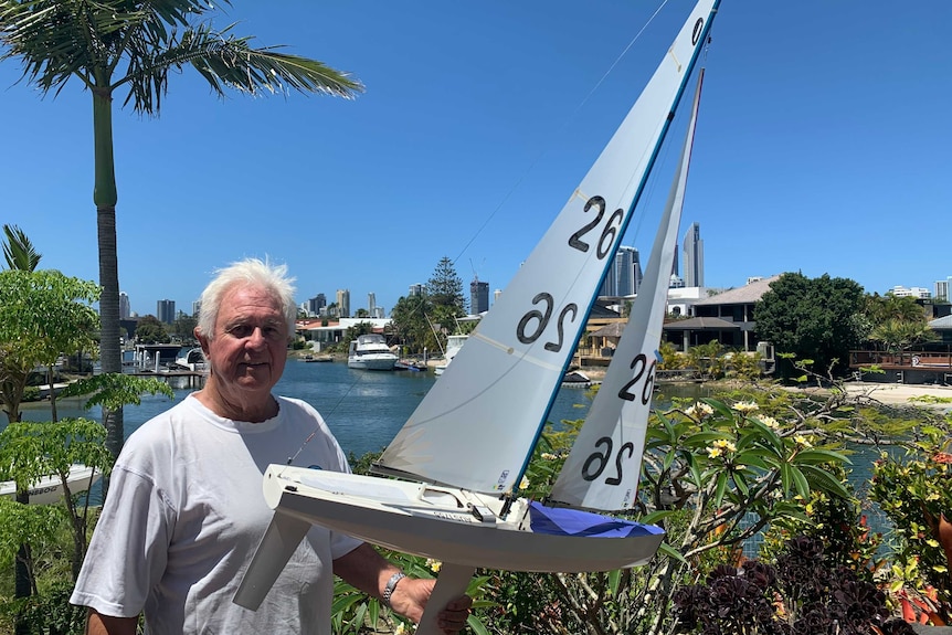 Radio yacht enthusiast Allan Walker holding his boat near a Gold Coast canal.
