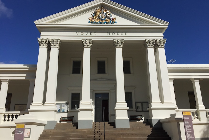 Large white building exterior with concrete steps and white pillars. Coat of arms visible up top with signage 'court house'