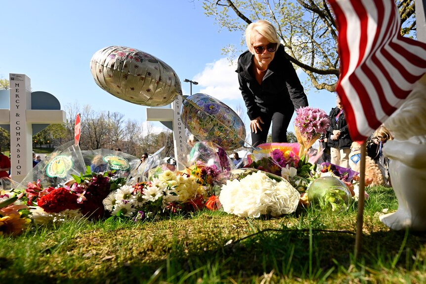 A woman places flowers at a memorial.