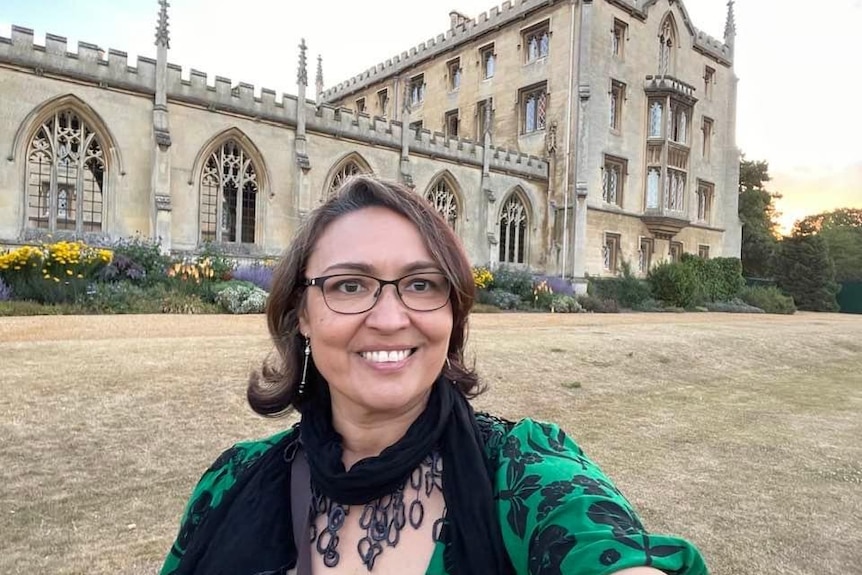 a woman with a pair of glasses on standing in front of an European chateau