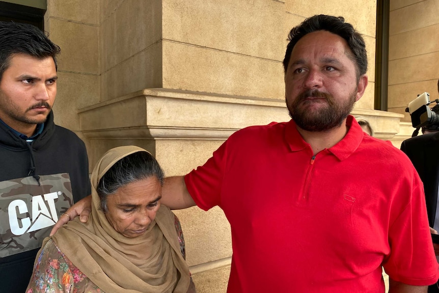 An Indian man with a beard in a red polo shirt next to a short older woman wearing a sari