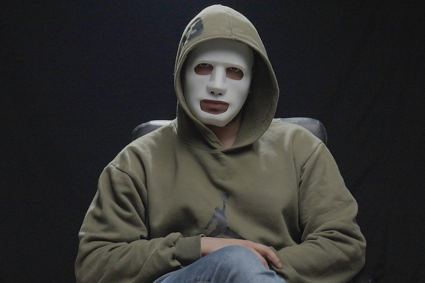 A man in a mask sitting on a chair.