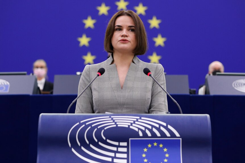 Sviatlana at a podium speaking in front of the EU flag