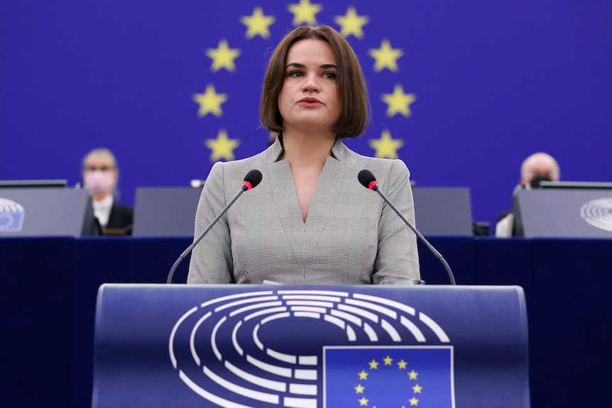 Sviatlana at a podium speaking in front of the EU flag