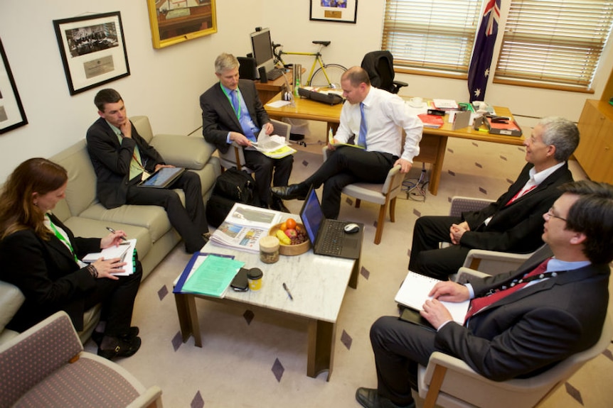 Five staffers are seen from above sitting around Josh Frydenberg in his office.