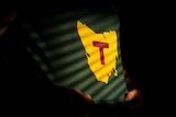A yellow map of Tasmania with a red capital T on a green background