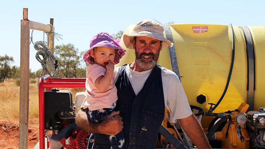 Grant Irving holding two-year-old Madeline, standing out the front of the family's work ute on Ethabuka Reserve.