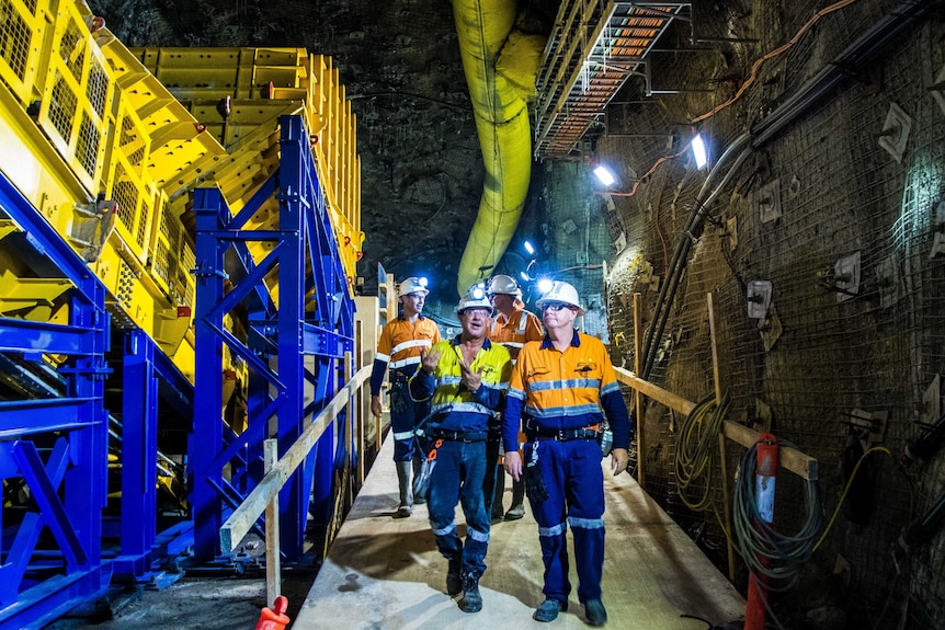 Men in hard hats walk through an underground mine