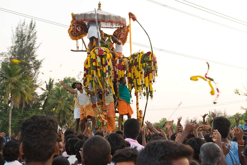Men throw marriage necklaces into the crowd from a tall effigy of an Indian god
