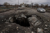 A large hole in the ground of a road with a car driving past.