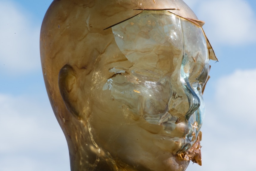 A human glass head model with peeling tanned film coming off the model's face.