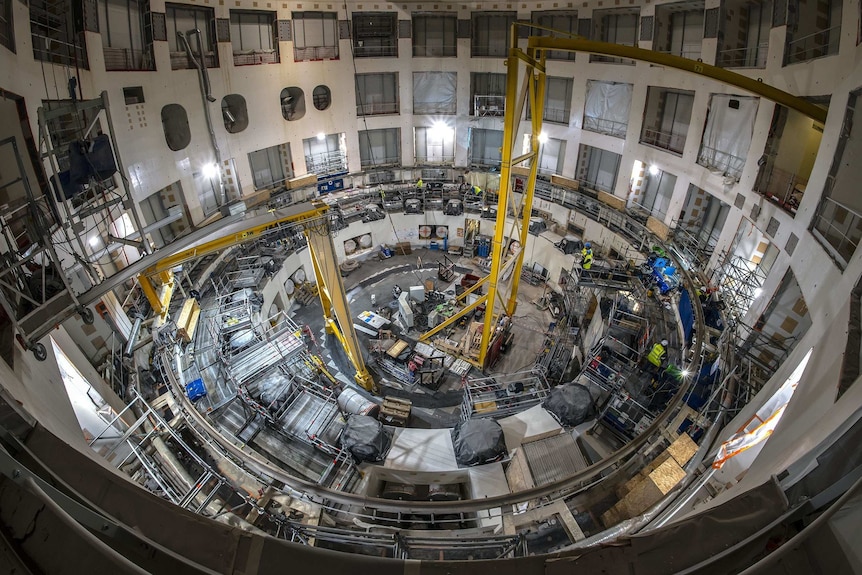 Inside an enormous cavity at the ITER site several stories high a number of people work amid scaffolding on the site.