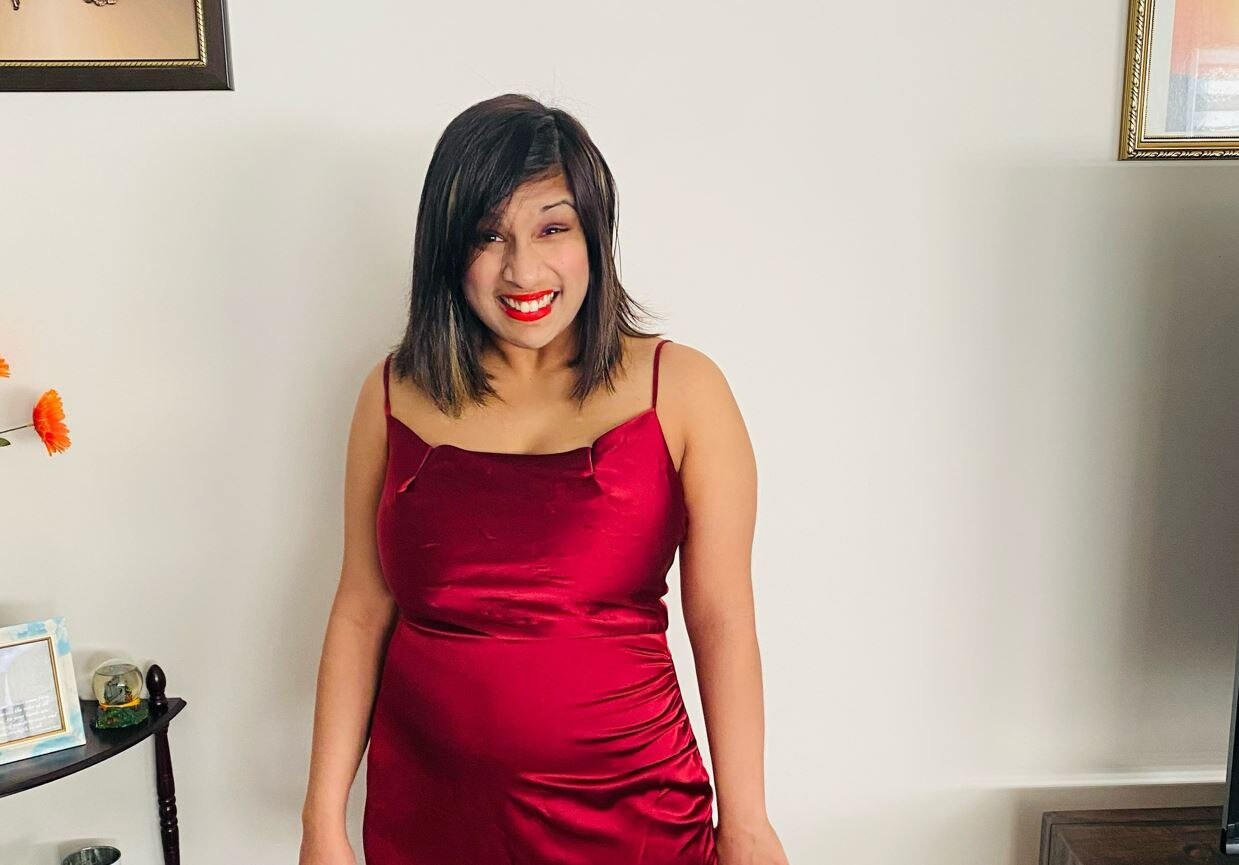 A woman smiling while wearing a silky red dress. 