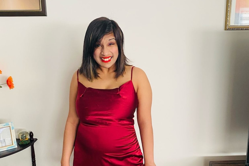A woman smiling while wearing a silky red dress. 