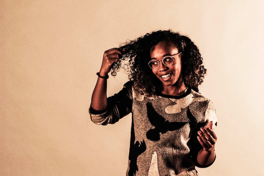 Body Portrait. Becky is holding tips of her curly hair out and smiling.