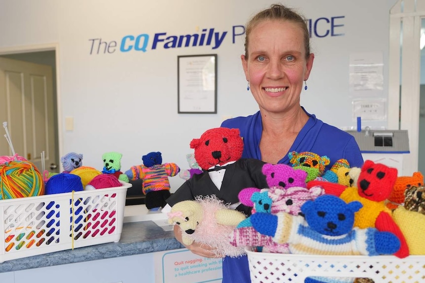 A woman smiles at the camera holding a box of colourful knitted bears.