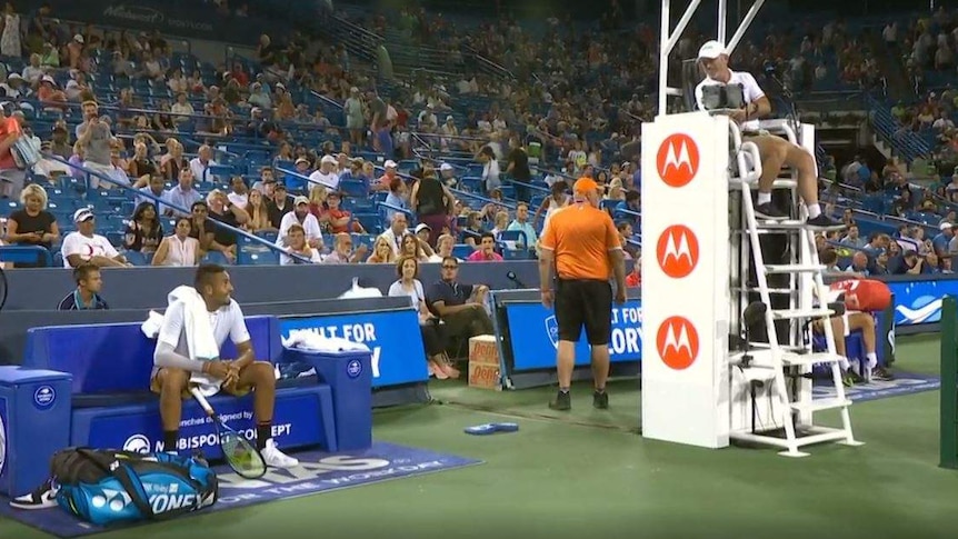 Kyrgios looks up and to his left to speak to the umpire, who is seated above and is looking down at Kyrgios.