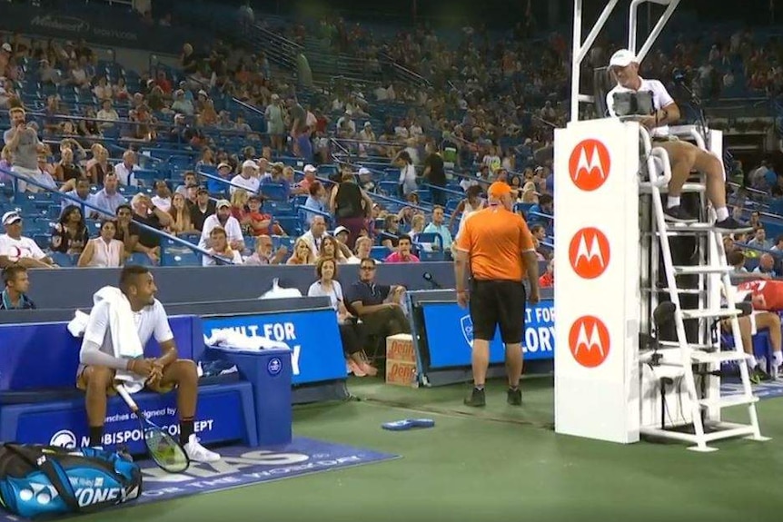 Kyrgios looks up and to his left to speak to the umpire, who is seated above and is looking down at Kyrgios.