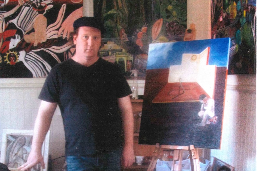 A man stands in a room surrounded by paintings.