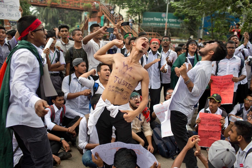 A group of students are seen shouting and one of them has the words 'we want justice' inscribed on his body.