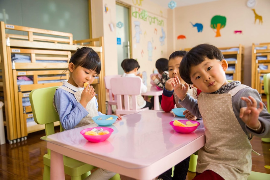 Three little kids sitting around a small table in a childcare centre