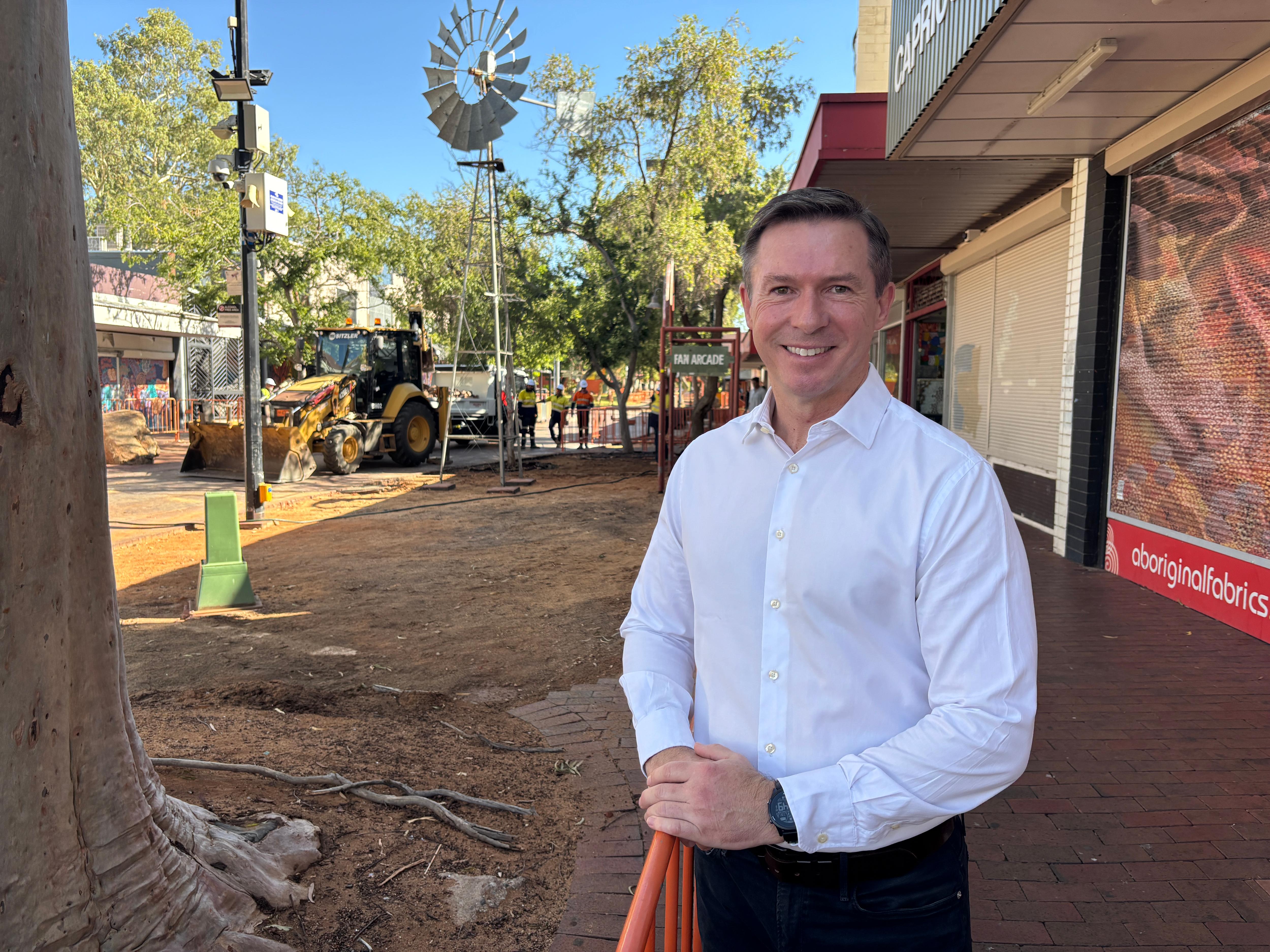 Um homem vestindo uma camisa branca está no Todd Mall, com uma construção ao fundo.