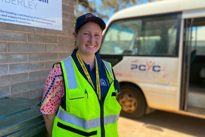 A smiling young girl with a hat and high vis on