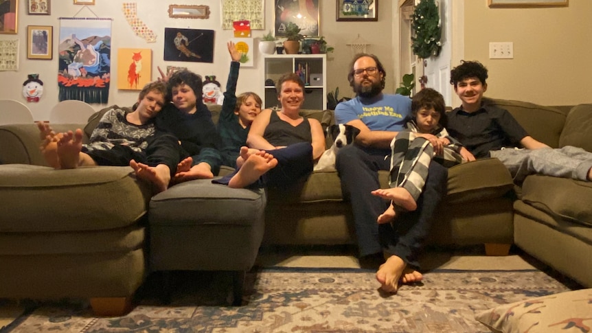 A family with five kids smiles on the couch. 