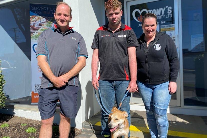 Two men and a woman stand smiling with a dog. 