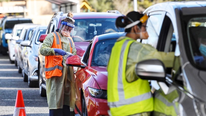 A woman in a hi-vis vest talks to the driver of a car in a long line of cars