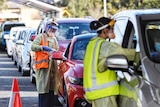 A woman in a hi-vis vest talks to the driver of a car in a long line of cars