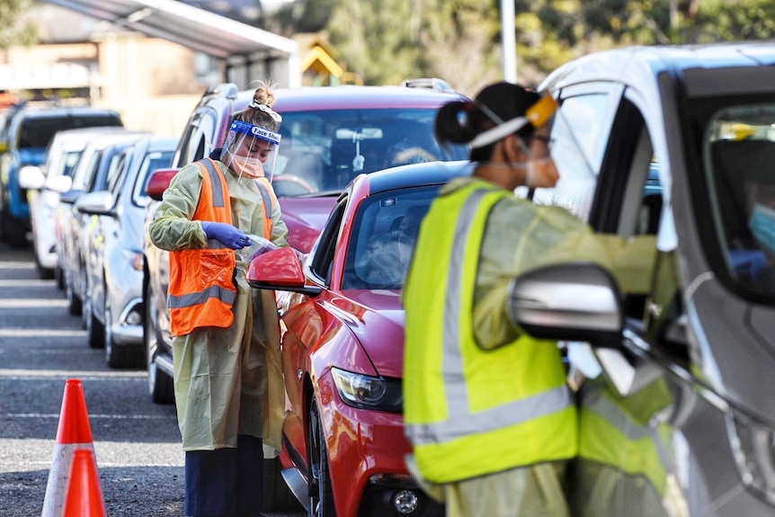 A woman in a hi-vis vest talks to the driver of a car in a long line of cars