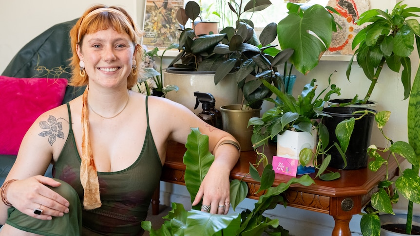 Woman wearing a dark green dress sitting beside a table full of indoor plants. 