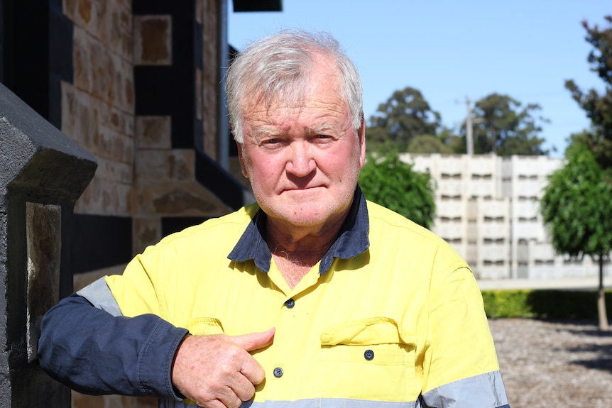 An older man in a high vis yellow work short looks directly into the camera.