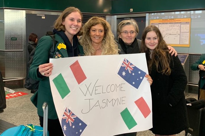 Jasmyne Paull stands with three women who hold a sign with the Italian/Australian flags which says "Welcome Jasmyne"