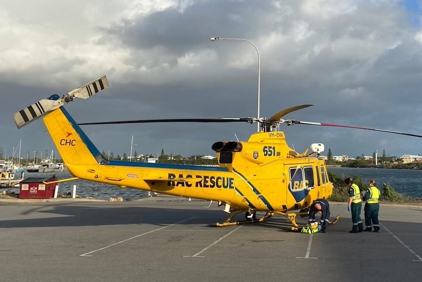 A large bright yellow RAC rescue chopper sits on the ground, people wearing high vis stand nearby.