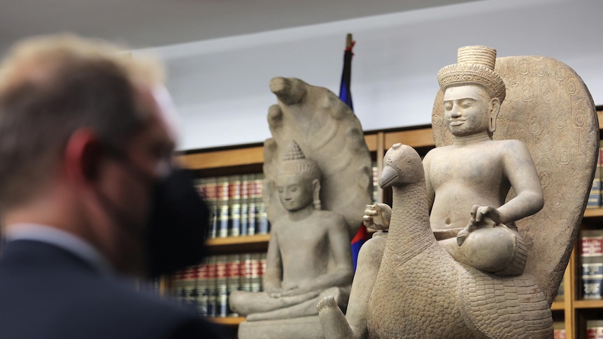 A person looks toward a seized 10th century Khmer sandstone statue of Skanda on a Peacock