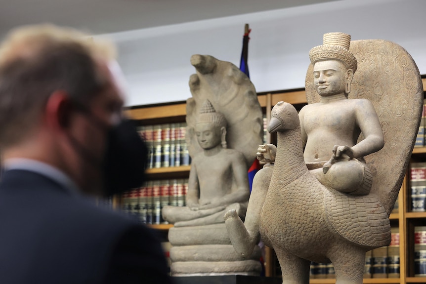 A person looks toward a seized 10th century Khmer sandstone statue of Skanda on a Peacock