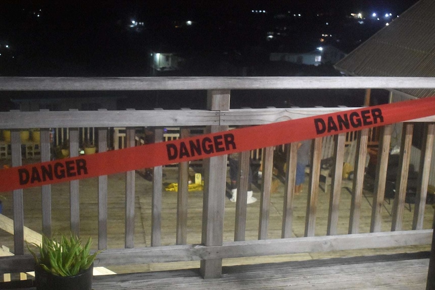 A fence with a danger sign across. Crime scene numbers can be seen behind the fence