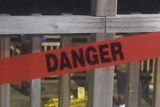 A fence with a danger sign across. Crime scene numbers can be seen behind the fence