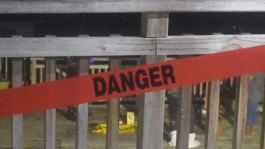 A fence with a danger sign across. Crime scene numbers can be seen behind the fence