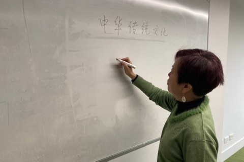 A woman stands at a whiteboard and writes in Chinese.