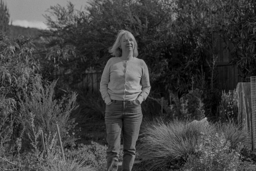 Woman stands in garden with hands in pockets 